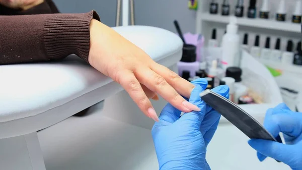 A manicura arquiva um prego com uma lima do prego a um cliente. Processo de manicure, extensão das unhas. close-up — Fotografia de Stock