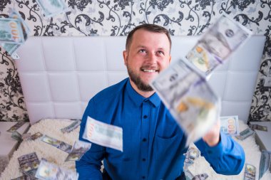 Mavi gömlekli bir adam beyaz yataktaki muazzam zenginliğe sevinir. Havada bir sürü para uçuşur..