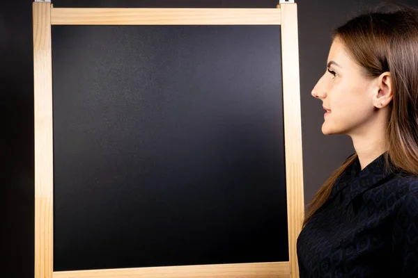 Female looks at an empty blackboard on which you can draw with chalk and write notes. Copy space — Stockfoto