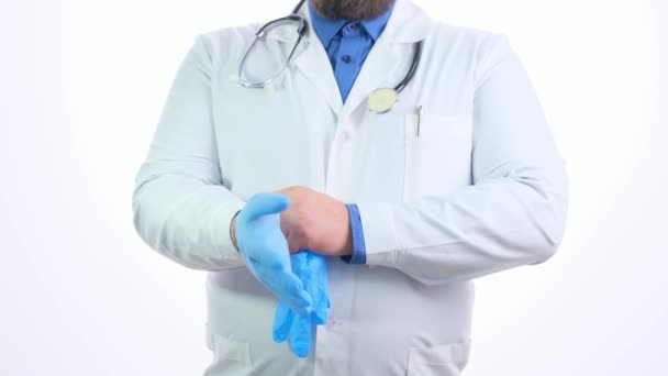 Лікар чоловік у білій формі тягне блакитні рукавички і знімає руку на білому тлі — стокове відео