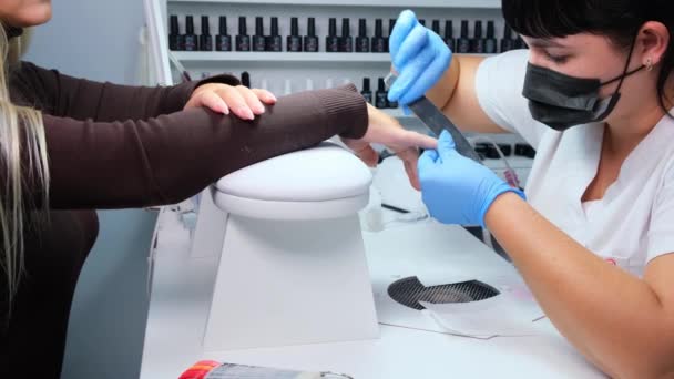 俄罗斯Nizhnevartovsk - 2019年8月12日：一名妇女在美甲店接受美容师指甲文件美容师的指甲修整。 女人在修指甲。 美容师给顾客的档案钉. — 图库视频影像
