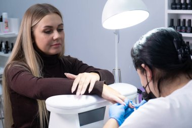  Güzellik salonunda hırdavatçı manikürü. Manikürcü kadın parmaklarına manikür yapmak için elektrikli tırnak matkabı uyguluyor.