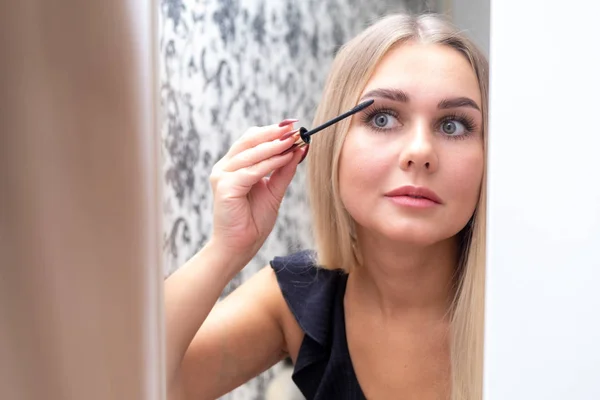Mulher aplicando maquiagem, pintar seus cílios, para uma data à noite na frente de um espelho — Fotografia de Stock