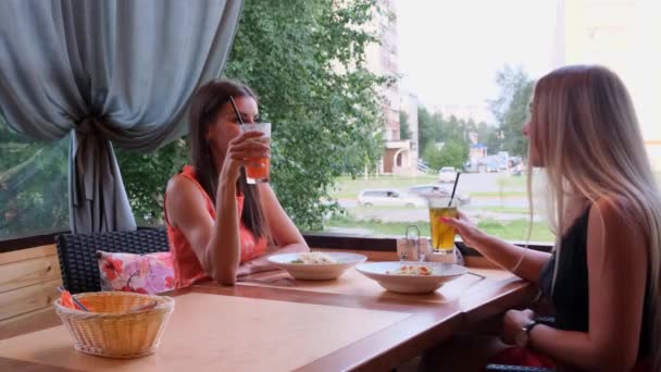 Dos chicas de pelo largo están descansando en un café con un interior moderno y riendo. Retrato interior de graciosas damas sonrientes en ropa de moda bebiendo batidos de frutas . — Vídeo de stock