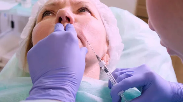 Lip augmentation. Beautician doctor doing a beauty procedure to female lips with a syringe. elderly woman. Lip augmentation.