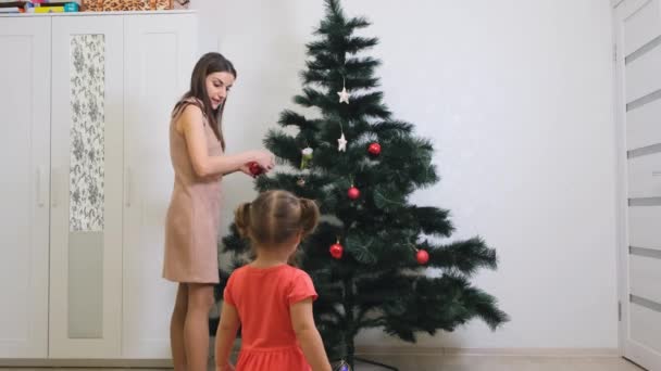 Madre felice e piccola figlia che decorano l'albero di Natale a casa. concetto di famiglia, vacanze invernali e persone . — Video Stock