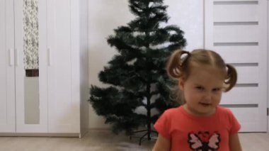 Küçük kız sırtı kameraya dönük duruyor ve Noel ağacına hayran. 2 yaşındaki bir kız ilk kez bir Noel ağacı görür ve sevinir. Peri masalına dalmak.