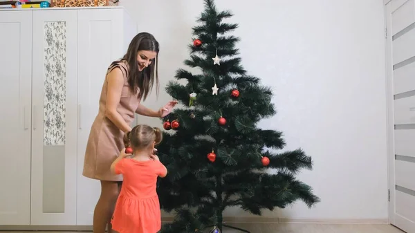 Familia, vacaciones de invierno y el concepto de la gente - madre feliz y la pequeña hija decorando el árbol de Navidad en casa — Foto de Stock