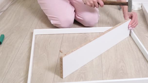 Жінка збирає білі меблі вдома за допомогою молотка. Крупним планом . — стокове відео
