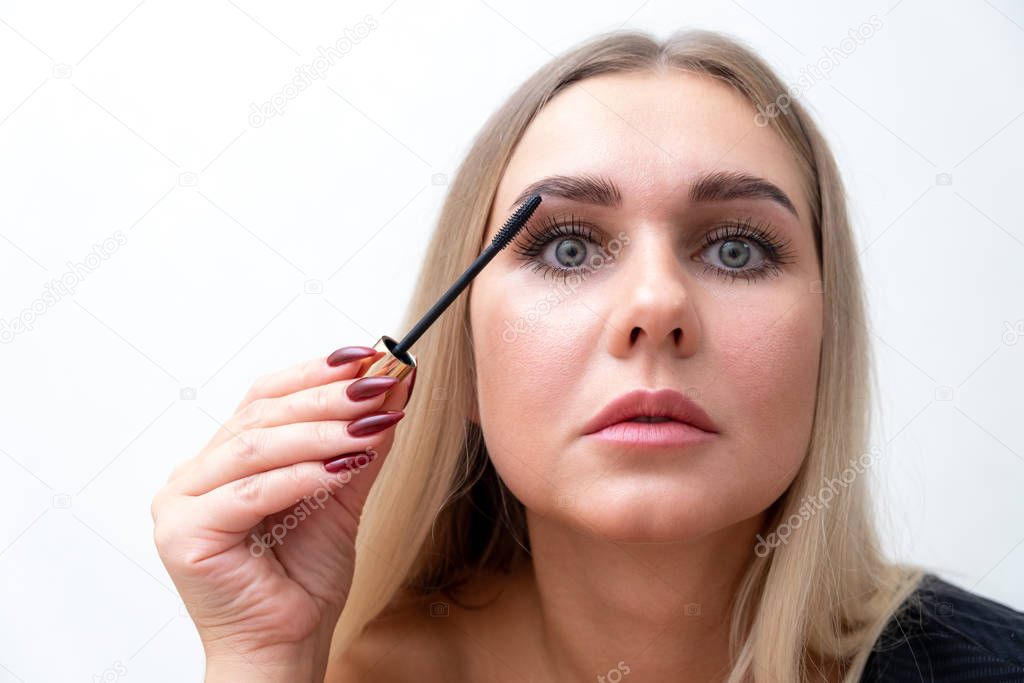 Headshot of female with bright makeup applying mascara on eyelashes.