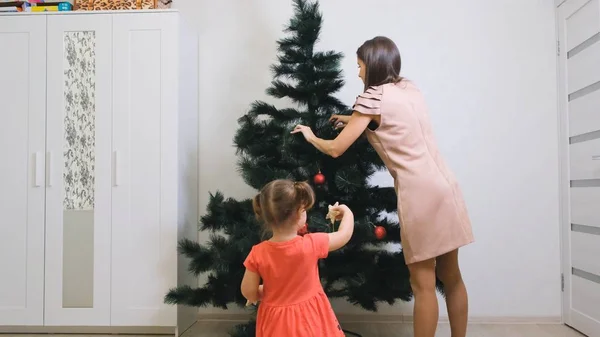 Feliz Navidad y Felices Fiestas. Mamá y su hija decoran el árbol de Navidad en el interior. La mañana antes de Navidad . — Foto de Stock