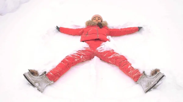 Woman in a red suit on the snow in a winter park makes the figure of a snow angel in the park. Copy space text — Stock Photo, Image