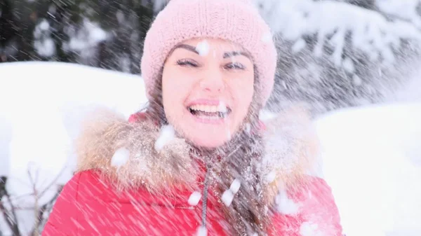 Jeune femme souriante en veste rouge jetant de la neige dans les airs par une journée d'hiver ensoleillée . — Photo