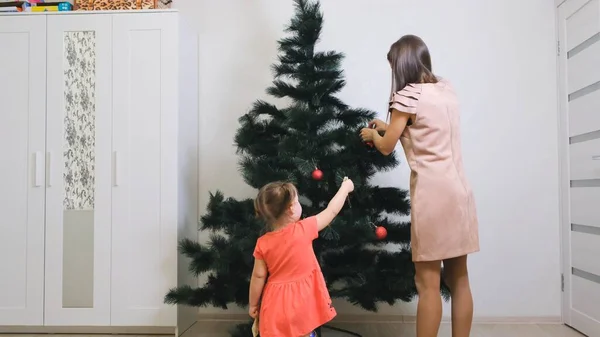 Lycklig mor och liten dotter dekorera julgran hemma. koncept familj, vinter semester och människor. — Stockfoto