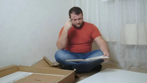 De bebaarde man verzamelt zelfstandig meubels in de woonkamer van zijn huis. De mens verzamelt meubels — Stockfoto