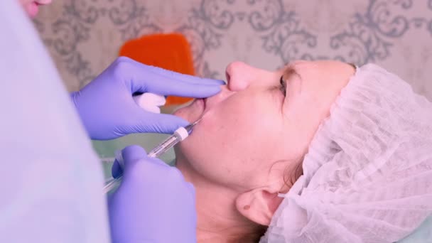 De cosmetoloog voert een procedure uit om de lippen van een vrouw te vergroten in een schoonheidssalon. huidverzorging. Cosmetische injecties. — Stockvideo