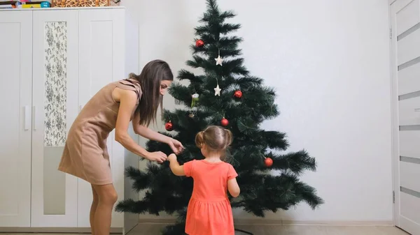 Feliz Navidad y Felices Fiestas. Mamá y su hija decoran el árbol de Navidad en el interior. La mañana antes de Navidad . — Foto de Stock