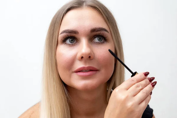 Beautiful blonde woman paints eyelashes. Beautiful female face. Makeup Read More Beauty girl with perfect skin. Makeup in progress — Stock Photo, Image