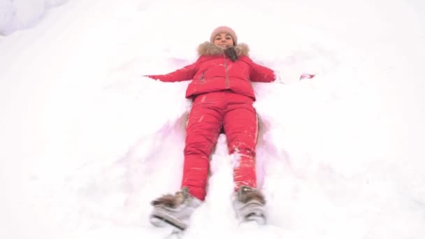 Woman in a red suit on the snow in a winter park makes the figure of a snow angel in the park. Copy space text — Stock Video