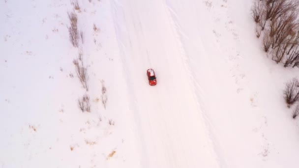 Oranje auto rijdt langs een winterbesneeuwde landweg. Luchtzicht vanuit de drone. — Stockvideo