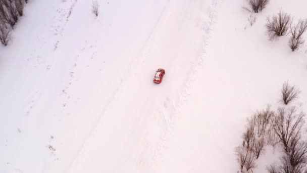 Ein orangefarbenes Auto fährt auf einer winterlich verschneiten Landstraße. Luftaufnahme aus der Drohne. — Stockvideo