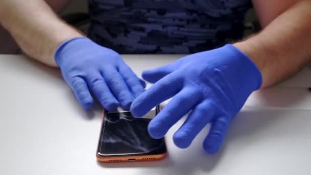 Αρσενικό χέρι σε μπλε γάντια αντικαθιστά ένα σπασμένο γυαλί ασφαλείας προστατευτικό οθόνης για ένα smartphone. Ένας άντρας ετοιμάζει ένα smartphone για να αντικαταστήσει το γυαλί. Έννοια επισκευής Smartphone — Αρχείο Βίντεο