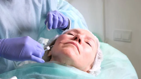Donna di mezza età 50 ottenere un'iniezione di sollevamento di un'iniezione di acido ialuronico in faccia da un cosmetologo medico. Procedura estetica. primo piano — Foto Stock