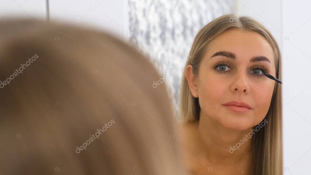 Woman Applying Make Up In Front Of A Mirror.