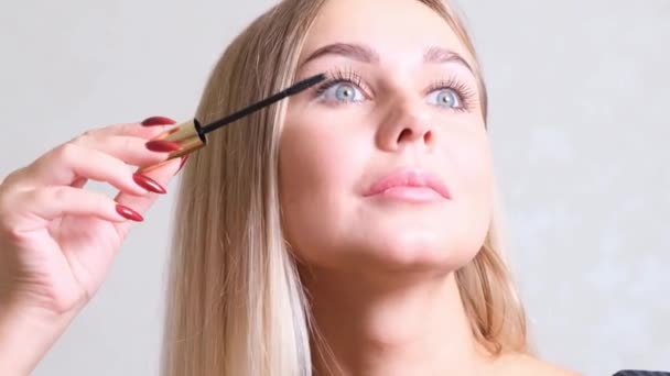 Vacker blond tjej med klassisk make up färger ögonfransar med mascara, poserar i studion. Skönhetsansikte. Vacker blond flicka med klassiska make-up färger. — Stockvideo