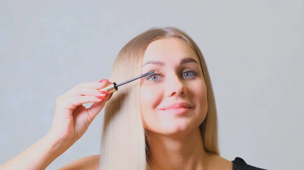 Maquiagem ocular. Mulher bonita aplicando rímel nas pestanas. Sorrindo fêmea fazendo pestanas make-up com escova . — Fotografia de Stock