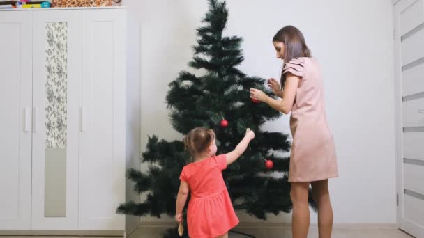 Veselé Vánoce a veselé svátky. Máma a dcera zdobí vánoční stromek uvnitř. Ráno před Vánocemi. — Stock video