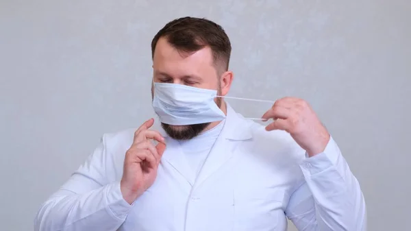 Il medico barbuto sta cercando di indossare una maschera protettiva. Concetto di igiene. prevenire la diffusione di germi e batteri ed evitare l'infezione con il virus della corona — Foto Stock