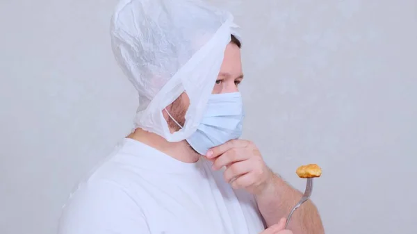 Vousatý muž v pytli na hlavě a ochranná maska má řízek z vidličky. Strach z infekce.Koronavirus COVID-19 Pandemie, domácí izolace a karanténa. — Stock fotografie