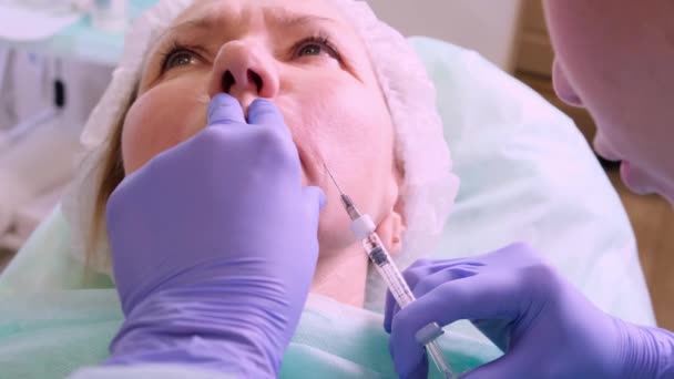 Женщина средних лет 50 лет получает подъемную инъекцию гиалуроновой кислоты в лицо от врача-косметолога. Косметическая процедура. макро — стоковое видео