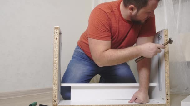 Uomo raccoglie indipendentemente mobili nel soggiorno della sua casa. L'uomo colleziona mobili. primo piano — Video Stock