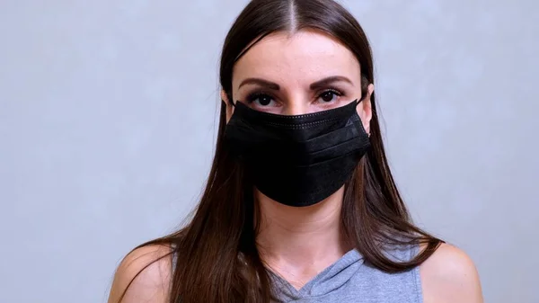Pacientka v jednorázovém víčku si nasadí černou ochrannou masku. Hygienický koncept. zabránit šíření bakterií a bakterií a vyhnout se infekci korunním virem — Stock fotografie