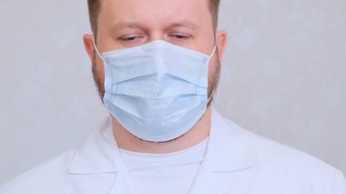 Üzgün ve üzgün koruyucu maskeli bir erkek ve beyaz bir gömlek kameraya bakıyor, yakın plan. Hijyen konsepti. Mikrop ve bakterilerin yayılmasını önlemek ve taç virüsünün bulaşmasını önlemek. Boşluğu kopyala