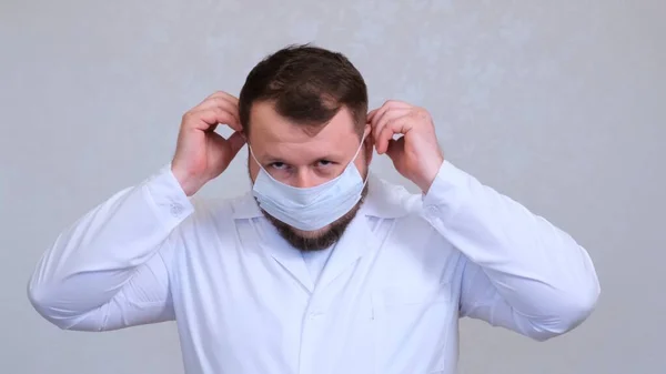 Szakállas férfi orvos próbál felvenni egy védő maszkot. Higiéniai koncepció. megakadályozza a baktériumok és baktériumok terjedését, és elkerüli a koronavírussal való fertőződést — Stock Fotó