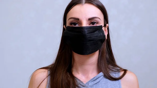 Pacientka v jednorázovém víčku si nasadí černou ochrannou masku. Hygienický koncept. zabránit šíření bakterií a bakterií a vyhnout se infekci korunním virem — Stock fotografie