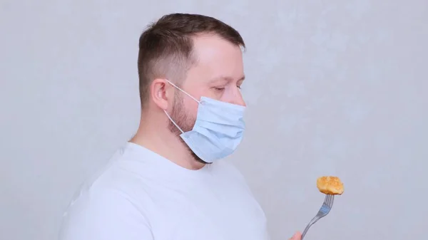 Male in a protective mask has a cutlet with a fork. Fear of infection. A joke situation. Copy space. Coronavirus COVID-19 Pandemic, home self-isolation and quarantine. — Stock Photo, Image