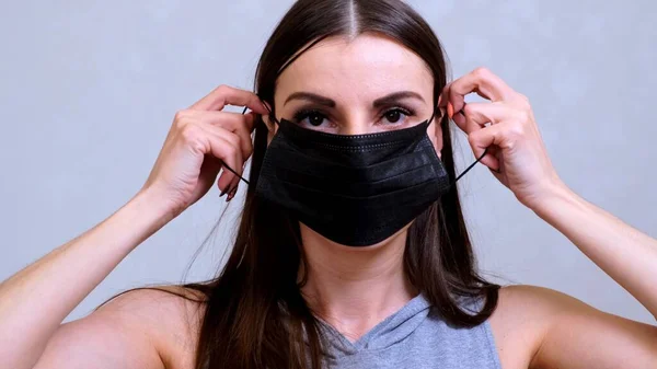 Kobieta zakłada czarną maskę ochronną. Koncepcja higieny. zapobiegać rozprzestrzenianiu się zarazków i bakterii oraz unikać zakażenia wirusem korony — Zdjęcie stockowe