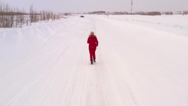 Θηλυκό τρέχει κατά μήκος ενός χειμερινού δρόμου ανάμεσα σε χιονισμένες χιονοπτώσεις και δέντρα, μια κορυφαία θέα που λαμβάνονται από ένα drone — Αρχείο Βίντεο