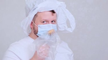 Maskeli sakallı bir adam ve kafasında bir torba pirzola yiyor. Enfeksiyon korkusu. Coronavirus COVID-19 salgını, kendini izole etme ve karantina. Sağlıklı beslenme yoluyla güçlü bağışıklık,