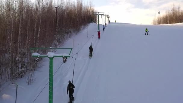 Подъем длится яркий зимний день. Лыжники и сноубордисты поднимаются на гору на лыжном подъемнике — стоковое видео