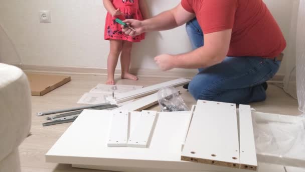 Papà uomo raccoglie mobili bianchi per la casa. La figlia aiuta papà a raccogliere mobili. primo piano — Video Stock