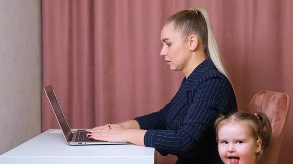 Mamá trabajadora trabaja en casa. Feliz madre e hija sonriendo. Mujer exitosa y un niño lindo usando el ordenador portátil. Trabajo freelancer. Asuntos femeninos. No es fácil, pero ella está a la altura —  Fotos de Stock