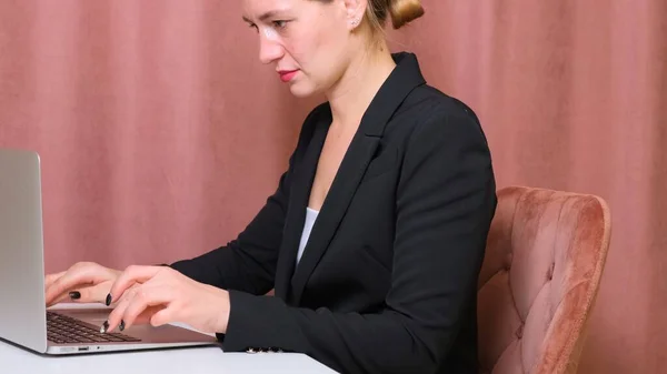 Frau benutzt Laptop, während sie an ihrem Schreibtisch sitzt. Junge europäische Geschäftsfrau sitzt im Büro und arbeitet an Notebook-Software. — Stockfoto