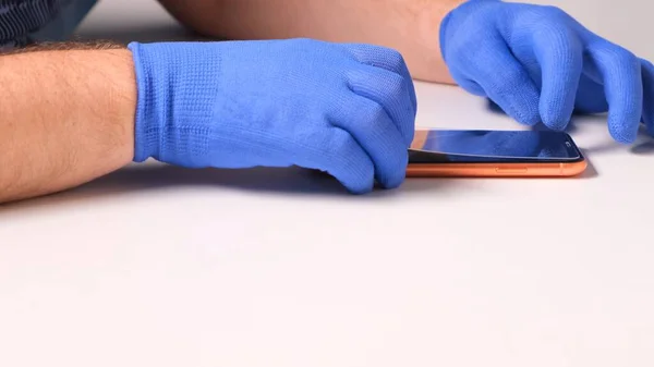 Manos masculinas en guantes azules reemplaza un protector de pantalla de vidrio templado roto por un teléfono inteligente. Un hombre prepara un teléfono inteligente para reemplazar el vidrio. Concepto de reparación de teléfonos inteligentes. espacio de copia —  Fotos de Stock