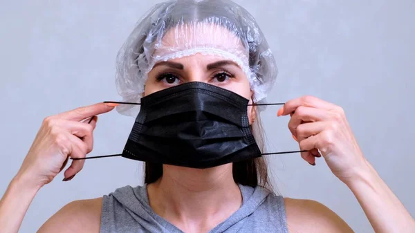 Paciente feminina em uma tampa descartável coloca uma máscara protetora preta. Conceito de higiene. prevenir a propagação de germes e bactérias e evitar a infecção com o vírus da coroa — Fotografia de Stock
