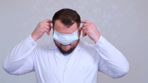 Бородатый врач-мужчина пытается надеть защитную маску неправильно на голову. Шутка. Понятие гигиены. предотвратить распространение микробов и бактерий и избежать заражения вирусом короны — стоковое видео